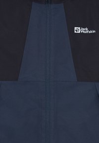 Giacca blu navy con zip frontale e spalle nere a contrasto. Tessuto texturizzato con un logo in alto a sinistra.