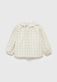 Blusa per bambini a maniche lunghe di colore crema con polsini elasticizzati, colletto arricciato e piccolo motivo floreale verde in motivi circolari.