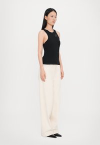 Black sleeveless top featuring a cutout detail, paired with high-waisted, loose-fitting cream trousers and pointed black shoes.