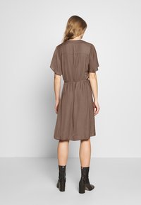 Brown polka dot dress with short flutter sleeves, belted waist, and knee-length hem. Worn with black heeled ankle boots.