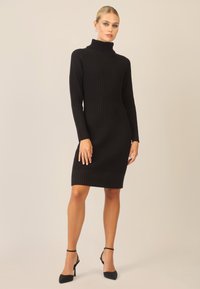 Schwarzes, geripptes Strickkleid mit hohem Ausschnitt und langen Ärmeln, das eine figurbetonte Silhouette und einen mittellangen Schnitt aufweist.