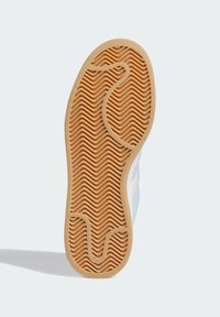 Rubber shoe sole featuring a textured, wavy pattern in caramel color; contours around foot for grip. Includes a smooth edge design.