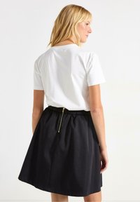 Svart kjol med samlad midja och en guldfärgad dragkedja på baksidan, kombinerad med en vit T-shirt med kort ärm. Slät tygstruktur.