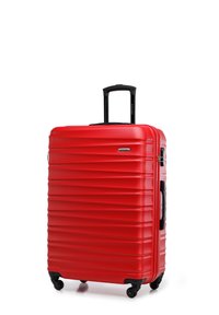 Valise rigide rouge avec une texture rainurée, poignée rétractable noire et quatre roues noires pour une mobilité facile.
