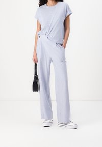 Světle modré pruhované tričko s uzlovým detailem, v kombinaci s pruhovanými širokými kalhotami a bílými teniskami. Černá kabelka v ruce.