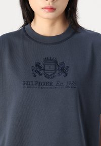 Marineblå sweatshirt med rund halsudskæring. Har et broderet logo med løver og teksten "HILFIGER Est. 1985" i en let hævet tekstur.