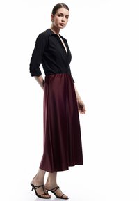 Sort skjorte med trekvartærmer, der går over i en burgunderfarvet, flydende nederdel, båret med sorte, ankelbundne hæle.