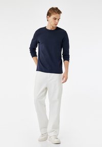 Camisa de manga larga azul marino, material suave, cuello redondo, ajuste relajado, combinada con pantalones blancos de pierna recta y zapatillas blancas, diseño minimalista.