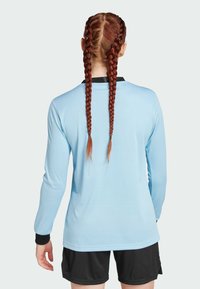Light blue long-sleeve shirt with ribbed texture, black collar, and cuffs. Model wears contrasting black shorts; hair is styled in two braids.