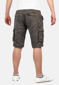 Grey cargo shorts with multiple pockets, unfinished hem, and a relaxed fit. Made from soft fabric, paired with white sneakers.
