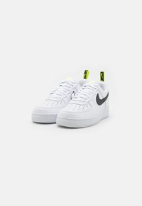 Vita Nike Air Force 1-sneakers med en slät läderöverdel, perforerat tåområde, svart swoosh och neongröna detaljer på hälflikarna.