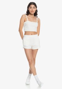 Hvid ribbet crop top med tynde stropper og matchende højtaljede shorts. Glat tekstur, minimalistisk design og lommer i shortsene.