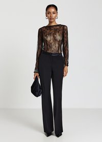 Body in pizzo nero con maniche lunghe, abbinato a pantaloni neri su misura. Gli accessori includono una borsa a mano in tessuto nero e décolleté a punta.