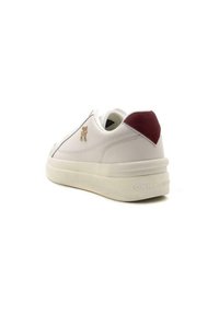 Sneaker bianco in pelle con accentuazione maroon sul tallone, punta arrotondata, texture liscia e "TOMMY HILFIGER" impressa sulla suola.