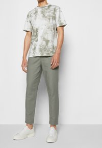 Zeleno-šedé tričko s batikovaným vzorem a kulatým výstřihem, spárované se světle zelenými zúženými kalhotami a bílými teniskami.