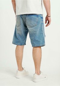 Ljusblå denimshorts med avslappnad passform, med fransiga kanter och två bakfickor. Bärs med vita sneakers.
