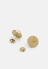 Boucles d'oreilles clous en ton or avec un design circulaire, présentant une texture lisse et un détail de logo gravé. Comprend une fermeture arrière assortie.