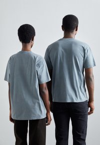 Camisetas de algodón azul claro con mangas cortas y un ajuste relajado, vistas desde la parte de atrás. Las camisetas presentan un escote simple y una textura suave.