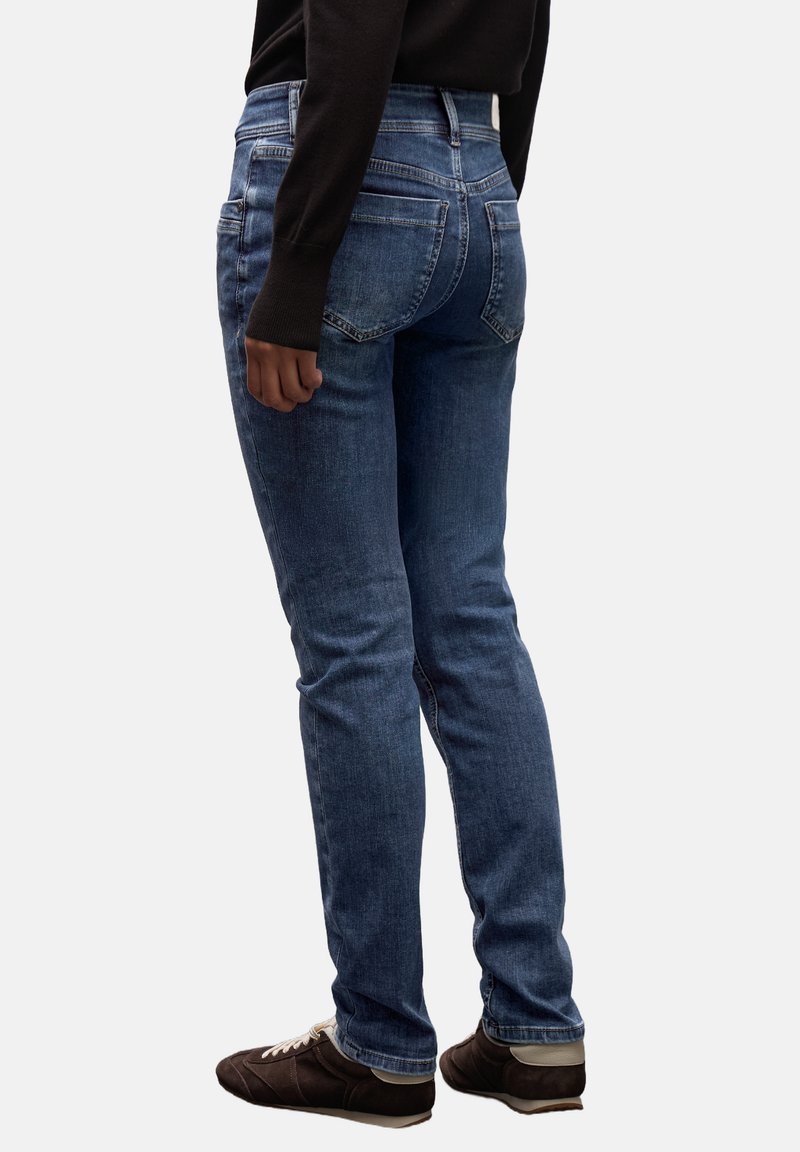 Jeans de color azul oscuro con un ajuste slim, diseño de cinco bolsillos y un ligero desgaste. Presentan una cintura de altura media y una tela con un poco de elasticidad.