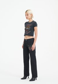 Black cropped t-shirt with tiger graphic and red accents paired with high-waisted black denim jeans featuring floral embroidery and straight leg cut.