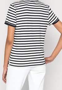 Koszulka z krótkim rękawem w biało-granatowe paski, z zaokrąglonym dołem i bocznymi rozcięciami. Materiał wydaje się miękki o gładkiej teksturze.