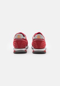 Scarpe da ginnastica rosse in suede con accenti grigi, dotate di un colletto imbottito, marchio distintivo nel tallone e una suola nera texturizzata.