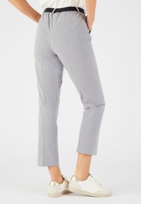 Grijze pantalon met krijtstrepen, een zwarte elastische tailleband, cropped lengte en achterzakken, gedragen met witte sneakers met gouden accenten.