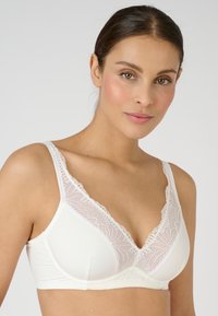 Witte beha met een diepe halslijn, voorzien van delicate kantafwerking langs de randen. De stof is glad en biedt een perfecte combinatie van comfort en verfijning.