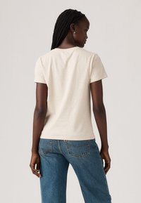 Beżowy bawełniany t-shirt z krótkim rękawem, okrągłym dekoltem i luźnym krojem, w połączeniu z niebieskimi dżinsami z wysokim stanem.