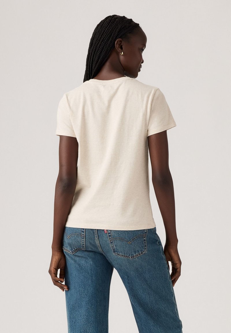 T-shirt en coton beige à manches courtes, col rond et coupe décontractée, assorti à un jean en denim bleu taille haute.