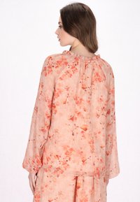 Perzikkleurige bloemenblouse met lange mouwen, geplooide halslijn, doorschijnende stof en delicate bloempatronen in tinten van oranje en roze.