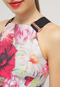 Robe à motif floral avec des couleurs vives rose, rouge et blanc. Bretelles noires avec détails en métal rose doré aux épaules.