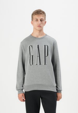 Grå hettegenser med rund hals og lange ermer. Har en stor, fet svart "GAP" logo på forsiden. Myk tekstur.