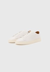 Pair of off-white low-top leather sneakers with cream soles and white laces on a plain light background.