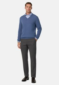 Šviesiai mėlynas megztinis su V-formos iškirpte, derinamas su pilkais suknelės kelnėmis. Išskirtinės detalės – kontrastuojančios rankogaliai ir rudos odinės bateliai.