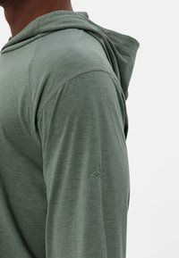 Felpa verde a maniche lunghe realizzata in tessuto morbido e leggero. Presenta un cappuccio, cuciture a costine e un logo discreto sulla manica sinistra.