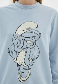 Sudadera de color azul claro con un gráfico de estilo cómic de un personaje femenino con cabello largo, vistiendo un vestido blanco y un sombrero, contorneado en negro.