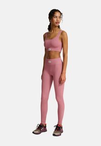 Roze geribbelde sportbra en legging set, met een strakke pasvorm en logo accenten. Model draagt veelkleurige trainingsschoenen.
