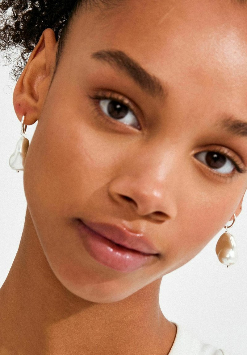 Perlenohrringe in Tropfenform mit einem Silberhaken. Die Perlen reichen von Creme bis Weiß und zeigen eine glatte, glänzende Textur.