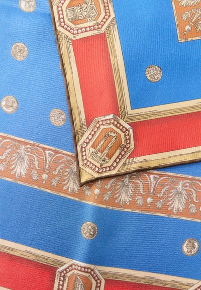 Μεταξωτό ύφασμα με περίπλοκα γεωμετρικά σχέδια σε κόκκινο, μπλε και μπεζ χρώμα, που περιλαμβάνει οκτάγωνα μοτίβα και διακοσμητικά σχέδια με χρυσά νομίσματα και λουλούδια.