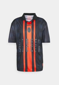 Camiseta de fútbol negra y roja con cuello, rayas verticales, texto "STREET SOCCER" y un logotipo centrado en el pecho.