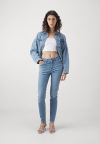 Ljusblå denimjacka och fina jeans, i kombination med en vit crop top och snörda vita sandaler. Slät textur, klassisk design.