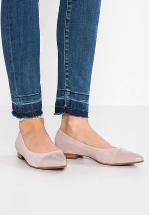 Lyserøde ruskindsballerinaer med en skinnende lædertåhætte, lav træhæle og rundet design, parret med slidte blå jeans.