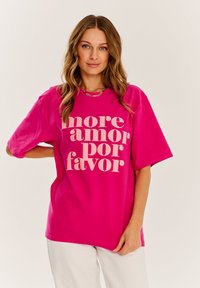 Fuchsie přerostlé tričko s výrazným světle béžovým nápisem "more amor por favor." Hladká bavlněná látka, volný střih, krátké rukávy.