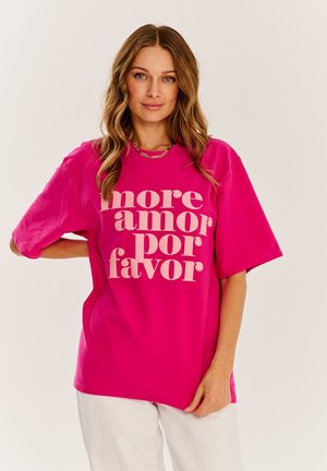 Fuchsie přerostlé tričko s výrazným světle béžovým nápisem "more amor por favor." Hladká bavlněná látka, volný střih, krátké rukávy.