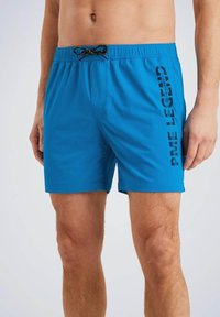 Shorts de bain bleus en tissu léger avec une taille élastique, un cordon de serrage marron et une impression de logo vertical noir sur le côté.
