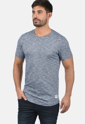 Heathered blå t-skjorte med rund hals og korte ermer, tettsittende design og en liten logo-tag på nederste søm. Brukt sammen med mørke jeans.