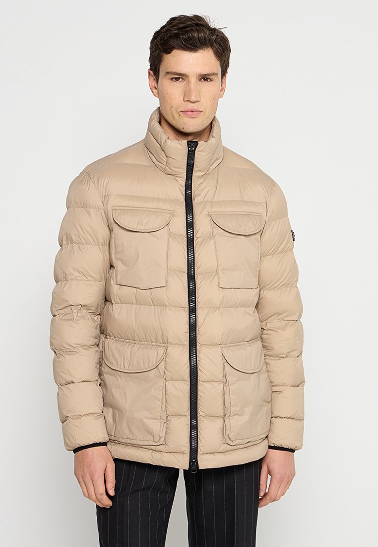 Beige puffjacka med hög krage, horisontell quiltning, två framfickor med lock och svart dragkedja.