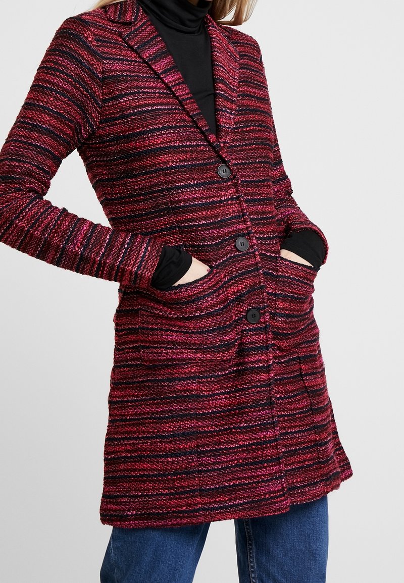 Cardigan a righe rosso e nero, lungo fino al ginocchio, realizzato in tessuto testurizzato, con colletto, sei bottoni e due tasche frontali.