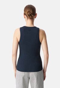Top sin mangas de canalé en azul marino con escote redondo y tirantes anchos. La parte trasera presenta un pequeño logotipo en el cuello. Combinado con pantalones a rayas.